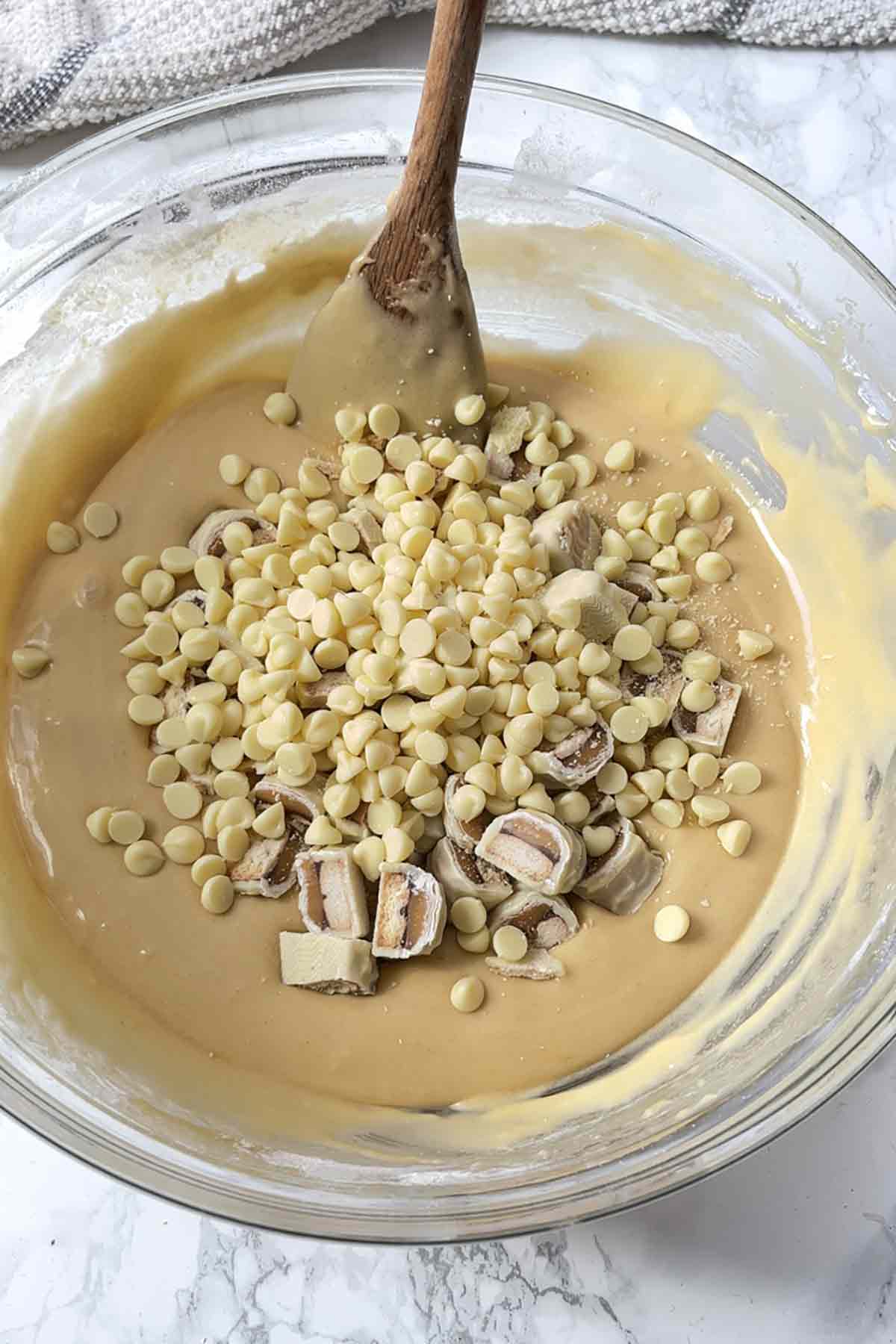bowl of batter with white twix pieces and white chocolate chips in it