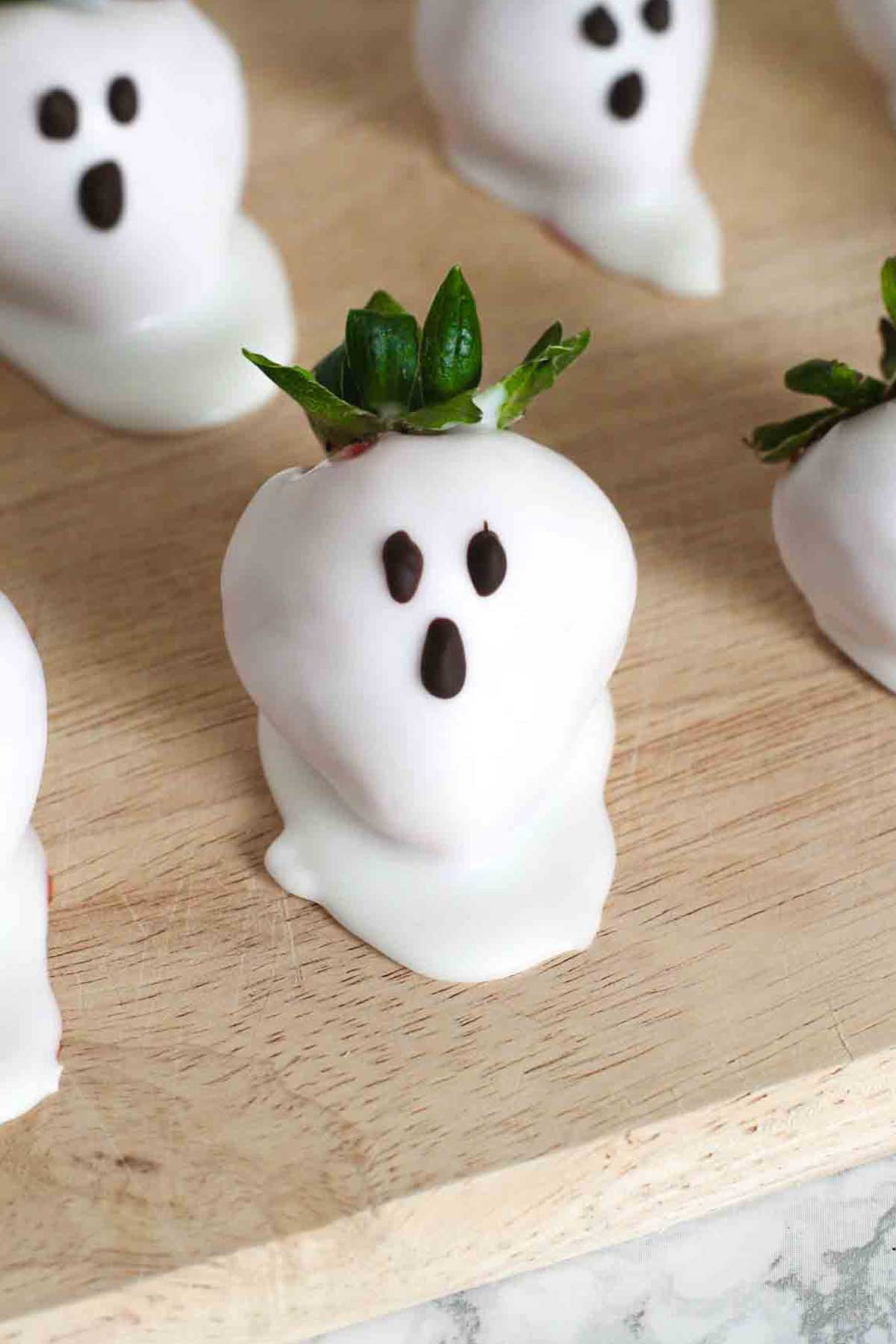 chocolate covered strawberry ghosts on a wooden board