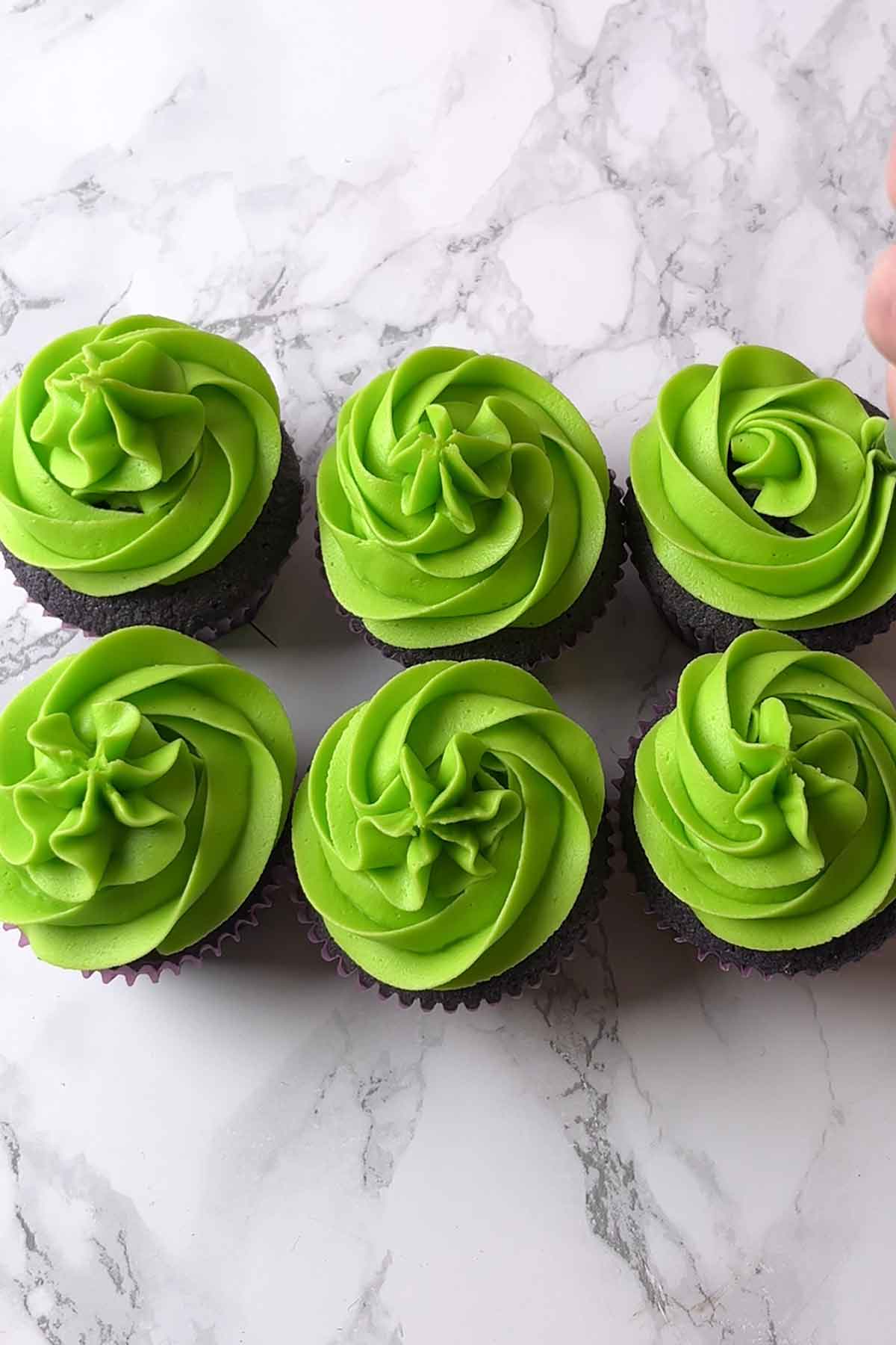 piping electric green frosting on top of the cakes