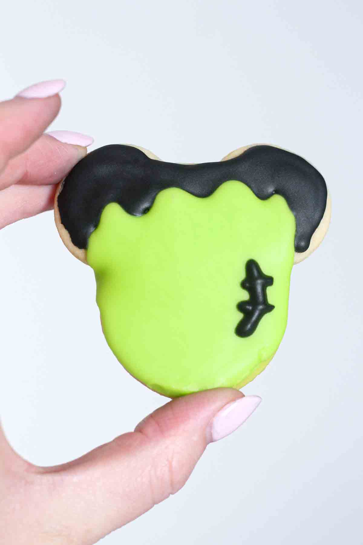 image of a hand holding up a frankenstein mickey mouse halloween cookie