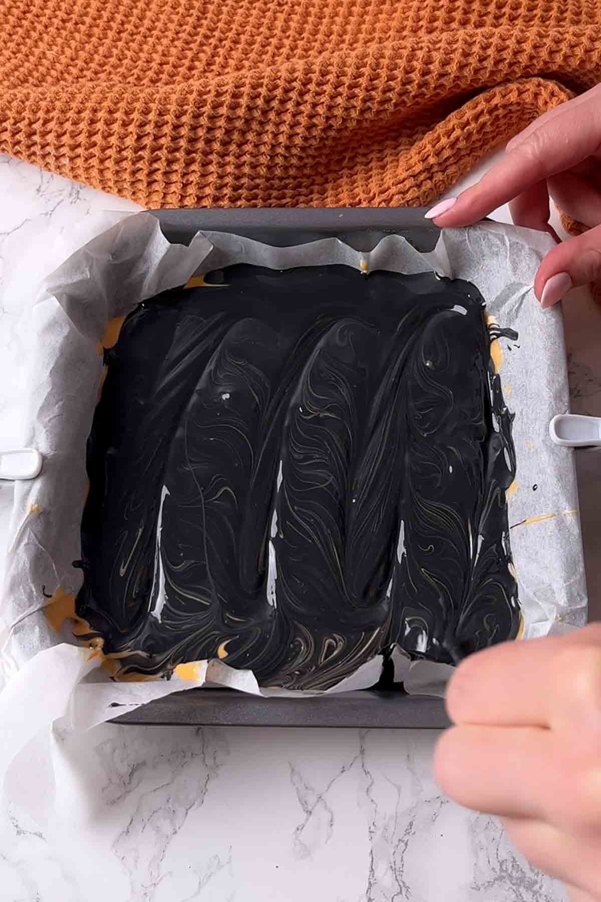 melted black chocolate on top of orange chocolate in tin