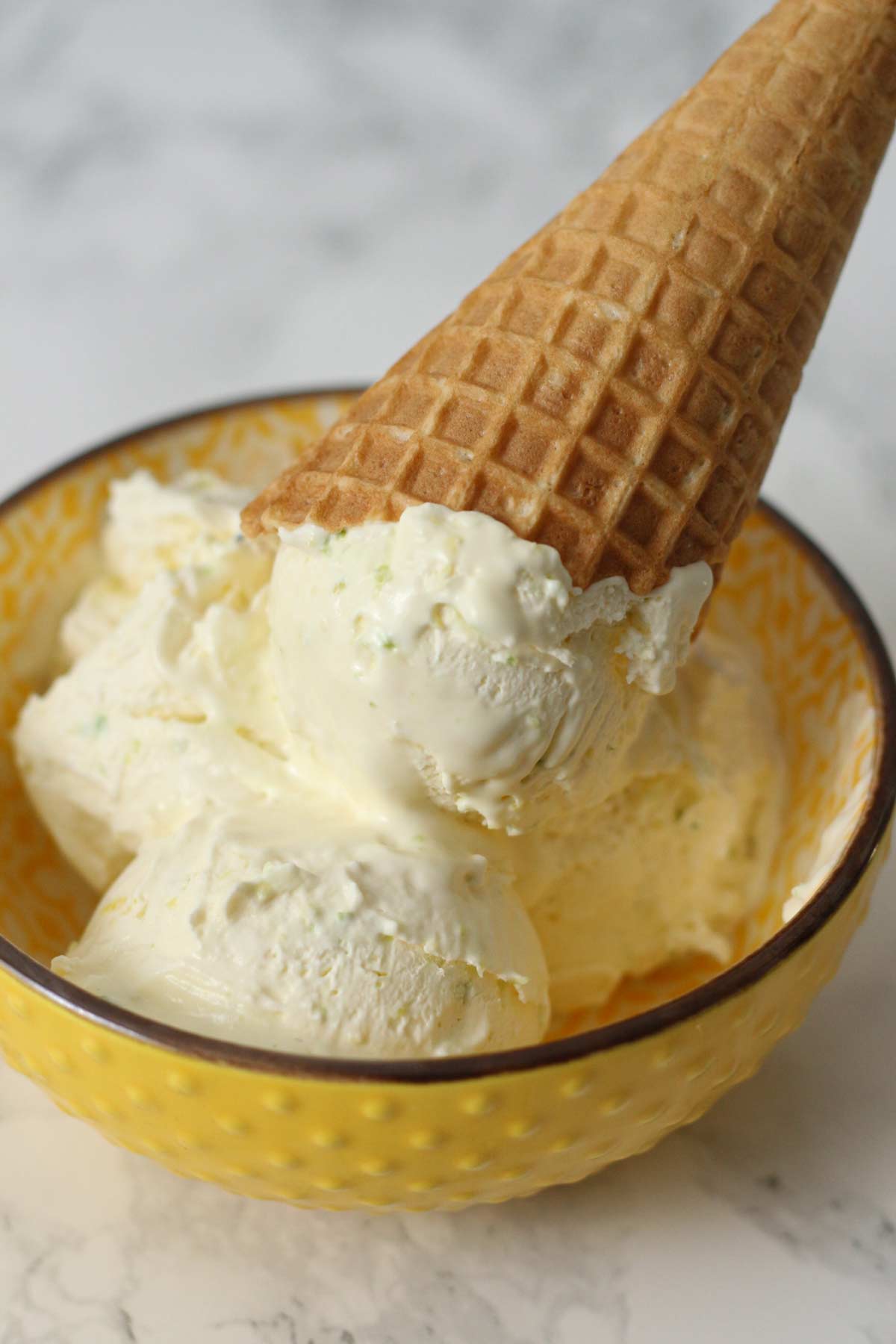 bowl of no churn lemon and lime ice cream with a waffle cone on top