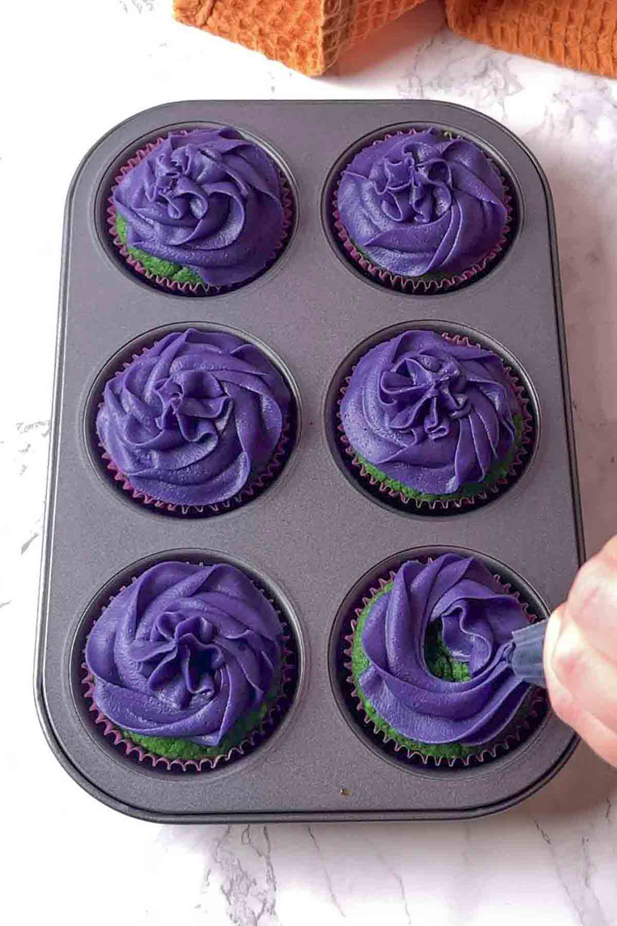 piping purple frosting onto the cupcakes