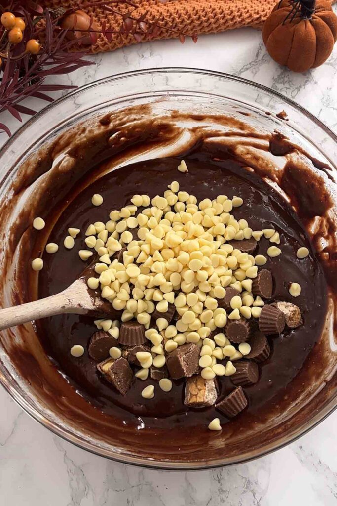 batter in a bowl with white chocolate chips snickers and reeses peanut butter cups
