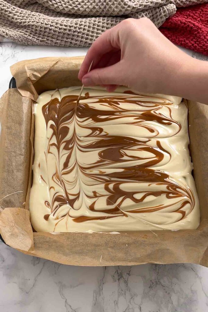 blending biscoff spread and white chocolate together with a toothpick