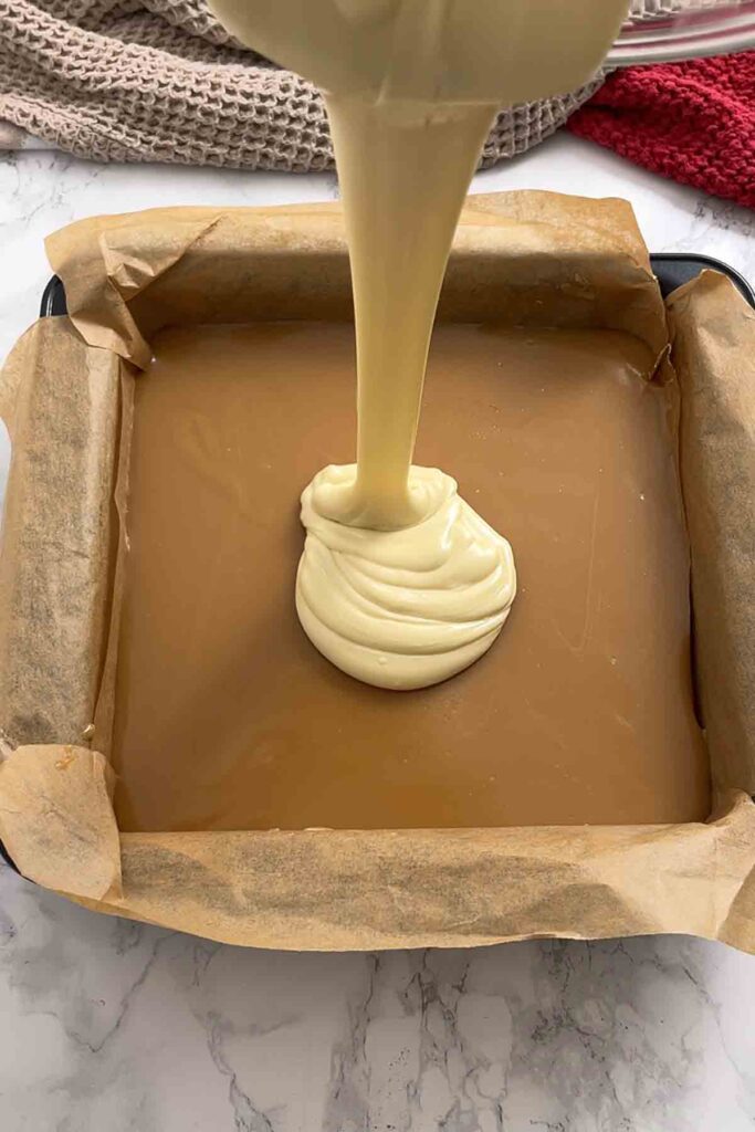 pouring white chocolate on top of the caramel