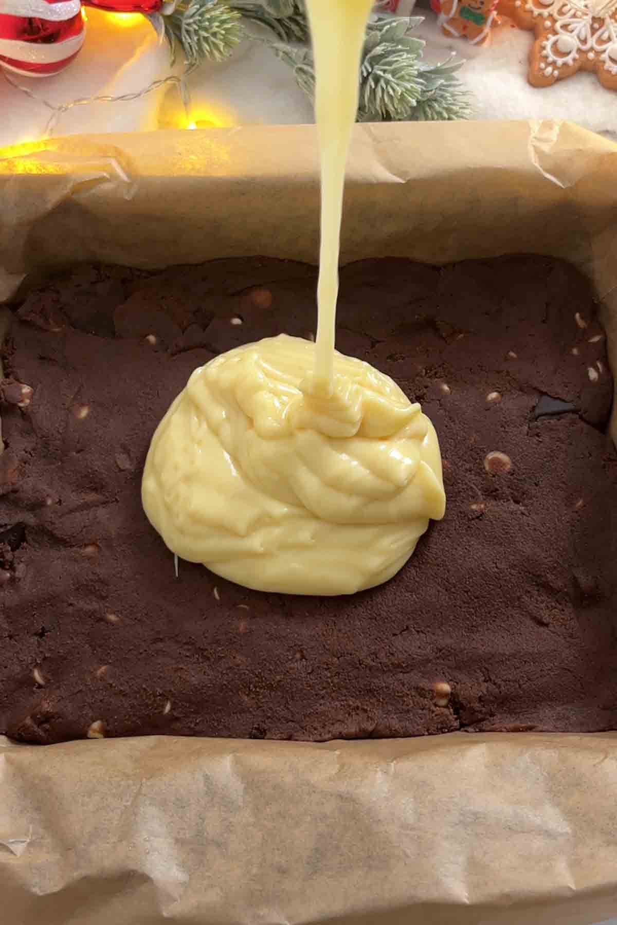 pouring white chocolate peppermint fudge on top of the cookie dough in the tin