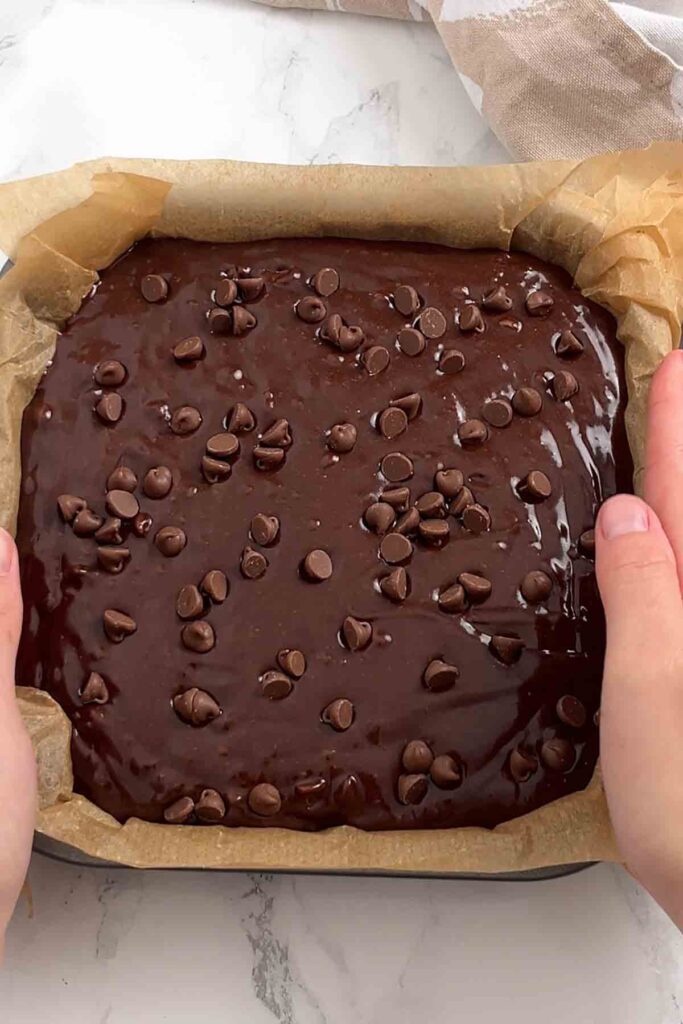 a lined tin of brownie batter with chocolate chips on top