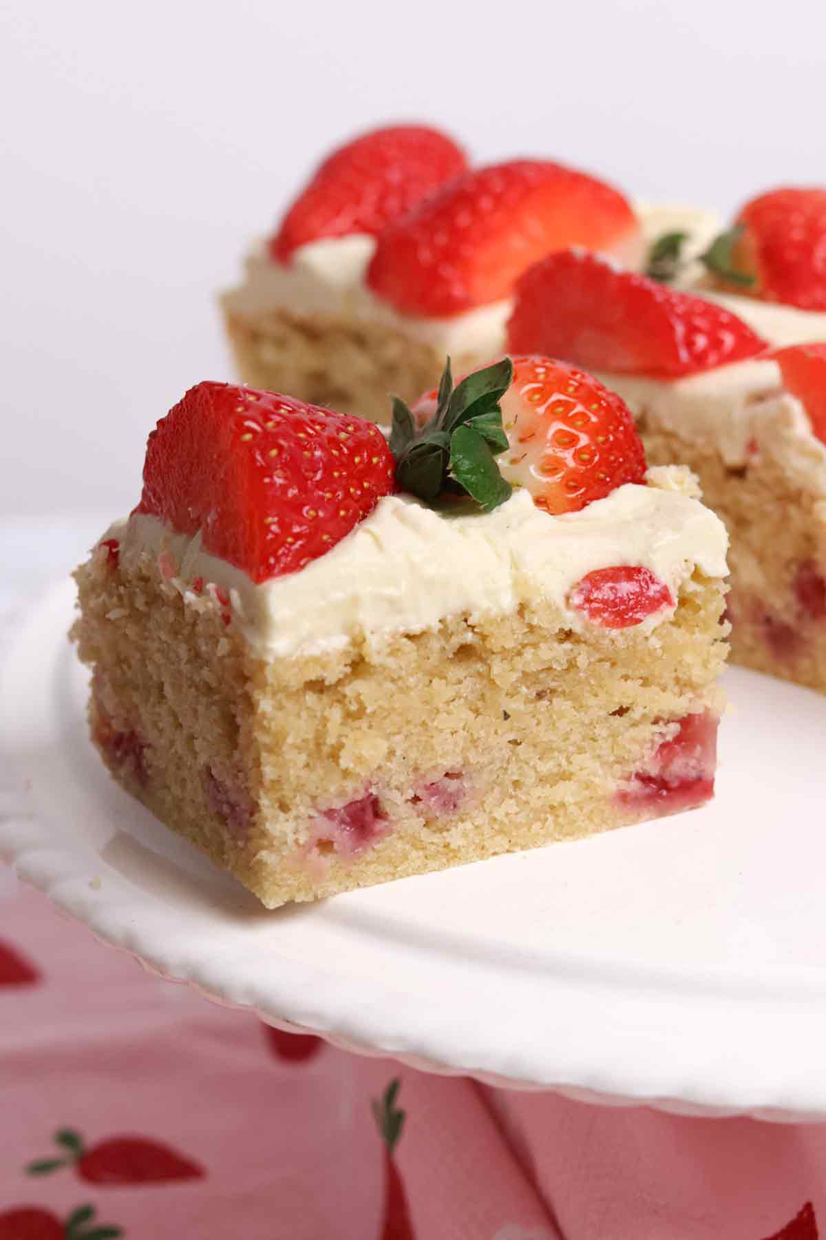 close up of a slice of strawberry white chocolate traybake on a cake stand
