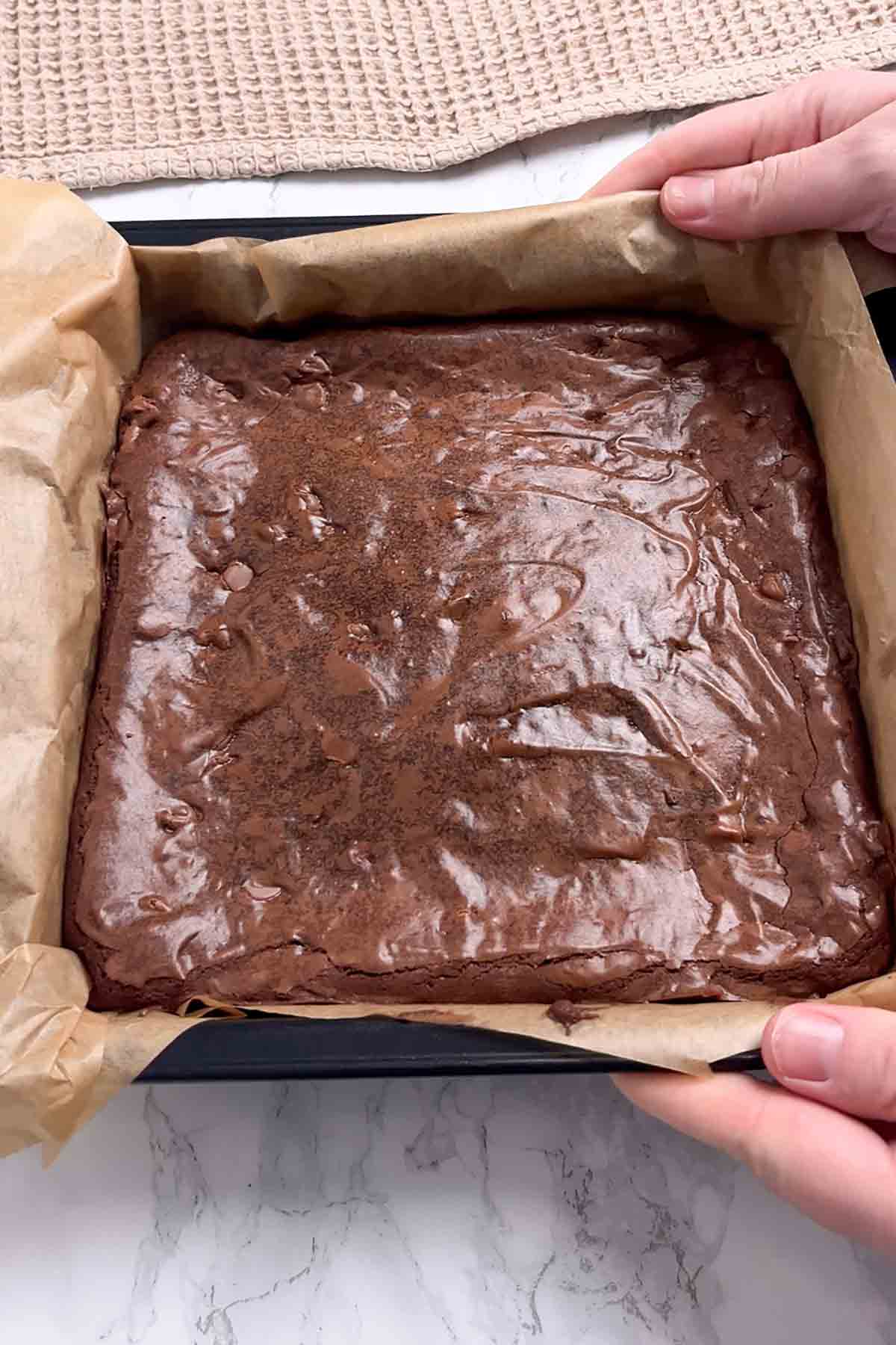 shiny baked brownie in a lined tin