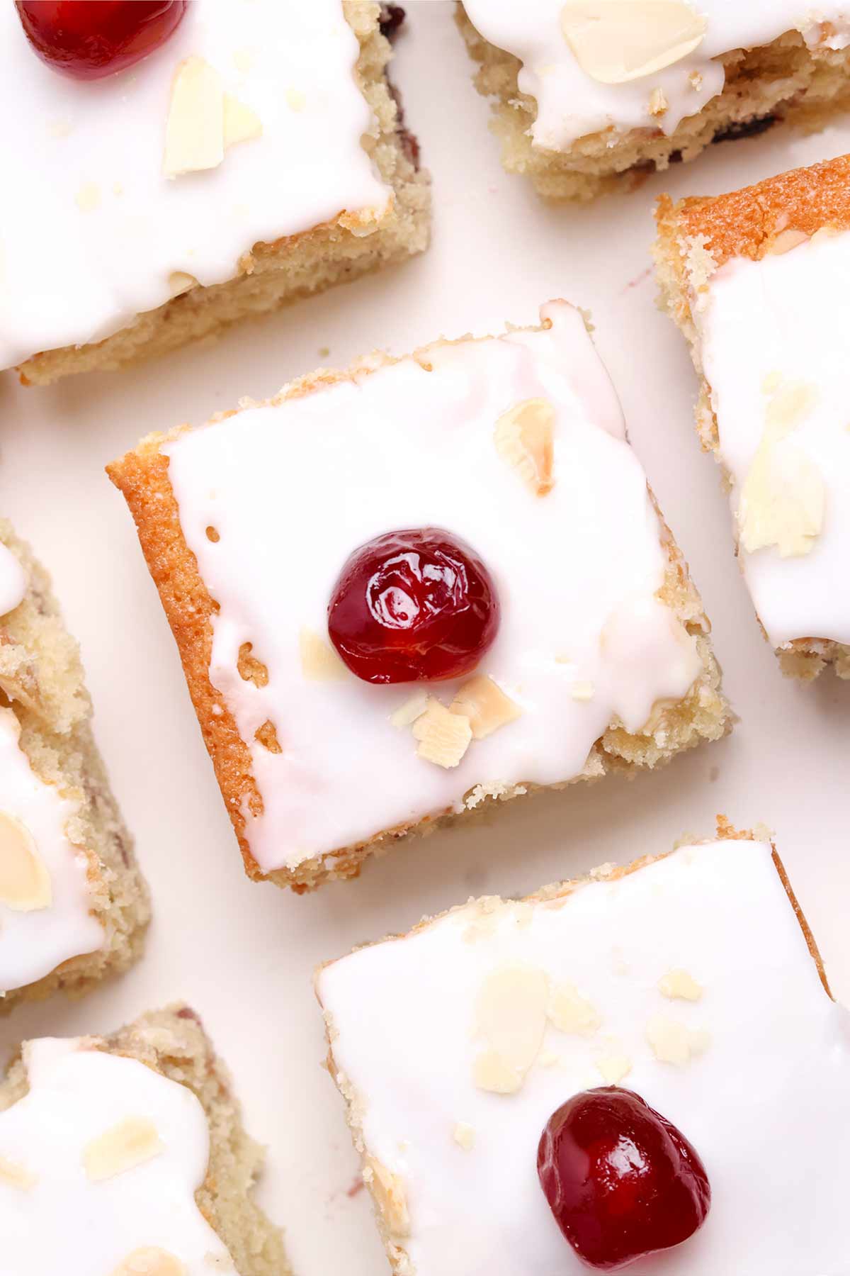 overhead image of cherry bakewell traybake cake slices on a white worktop