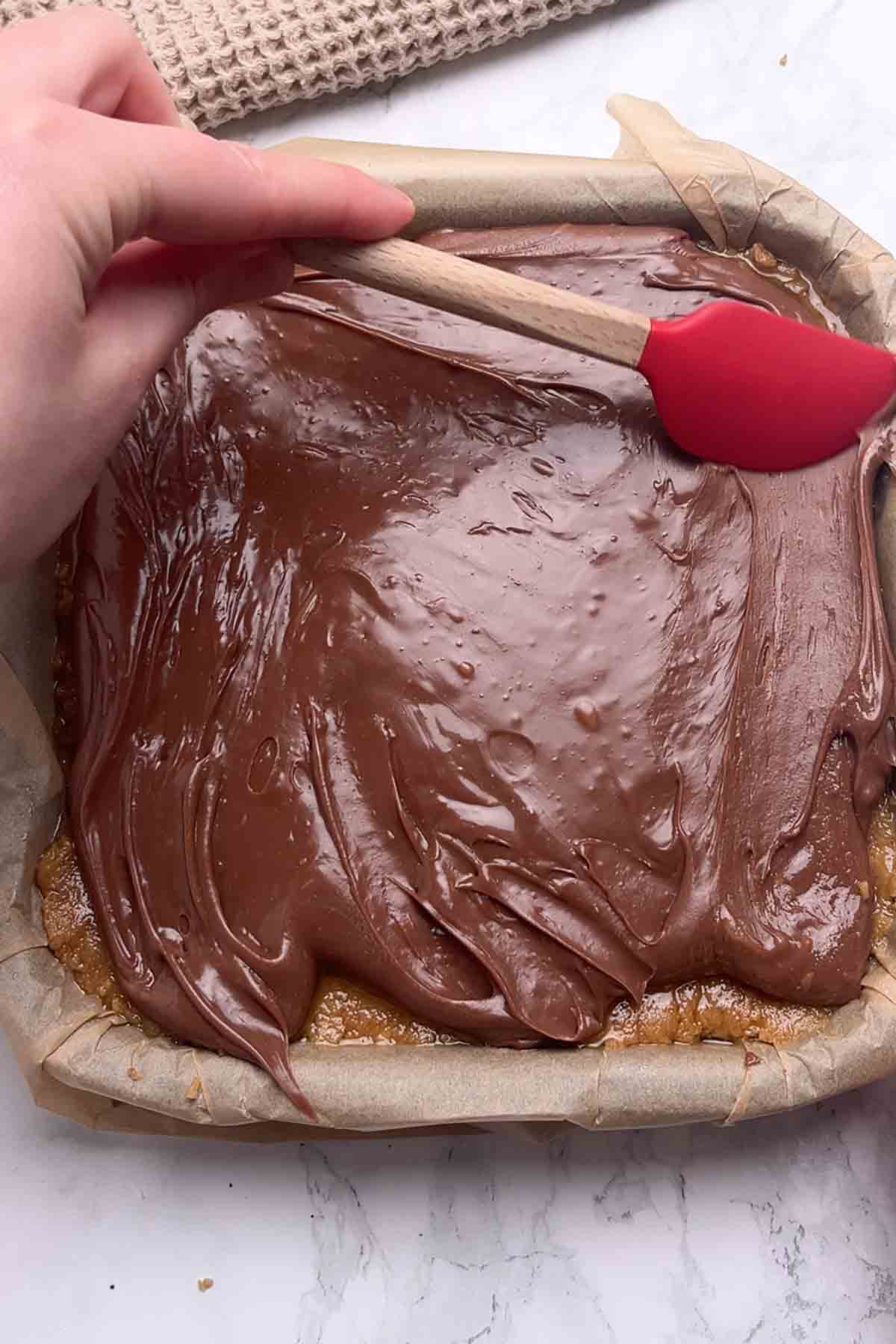 spreading chocolate fudge on top of the biscuit base