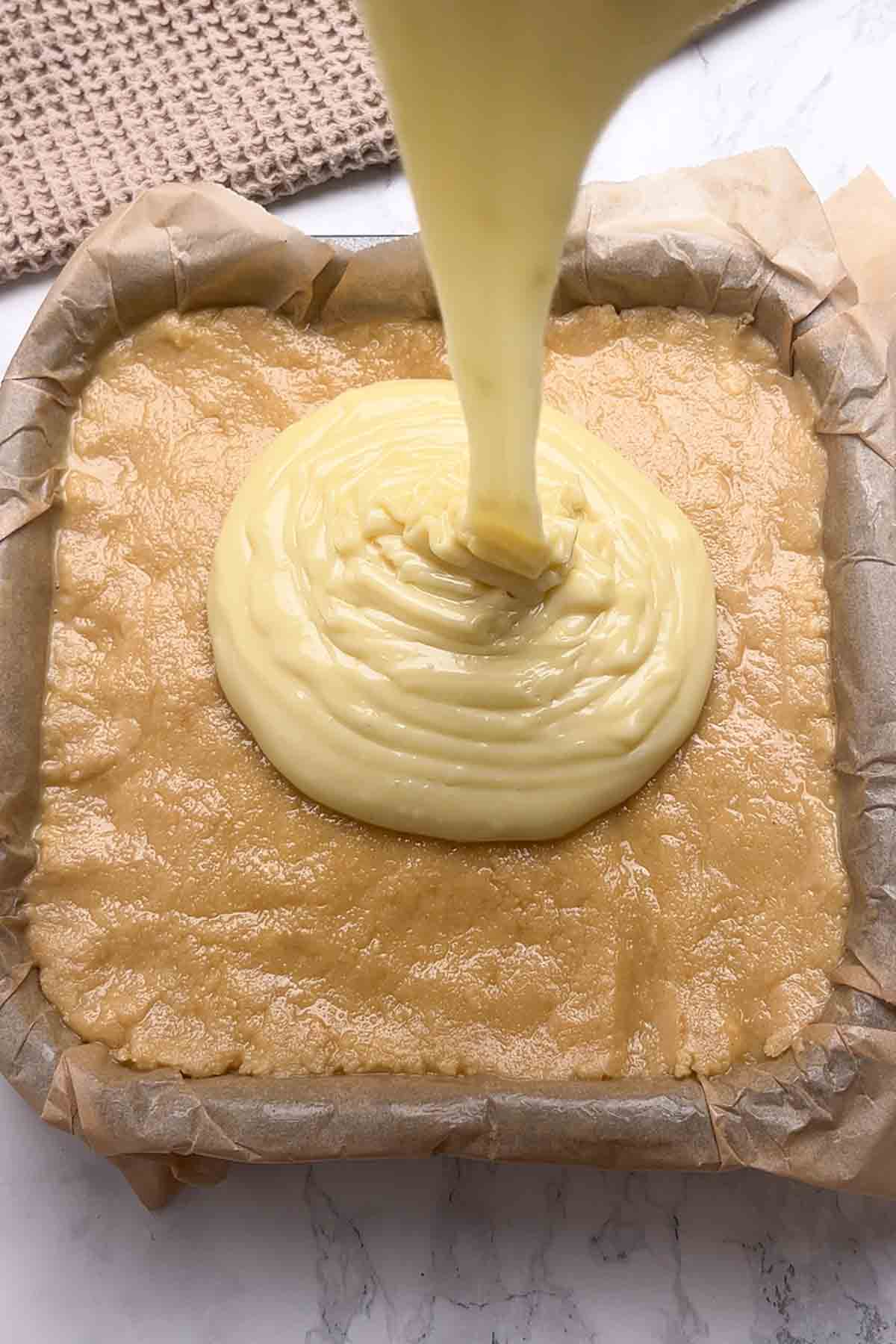 pouring white chocolate fudge onto the condensed milk biscuit base