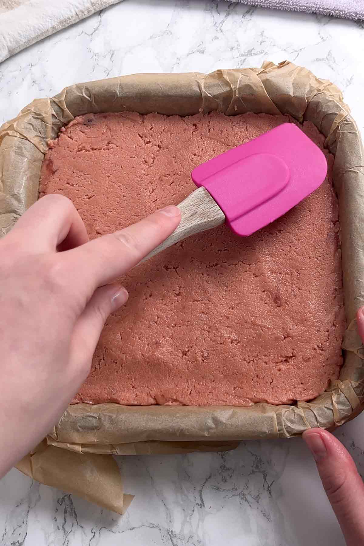 pressing pink biscuit base into lined tin