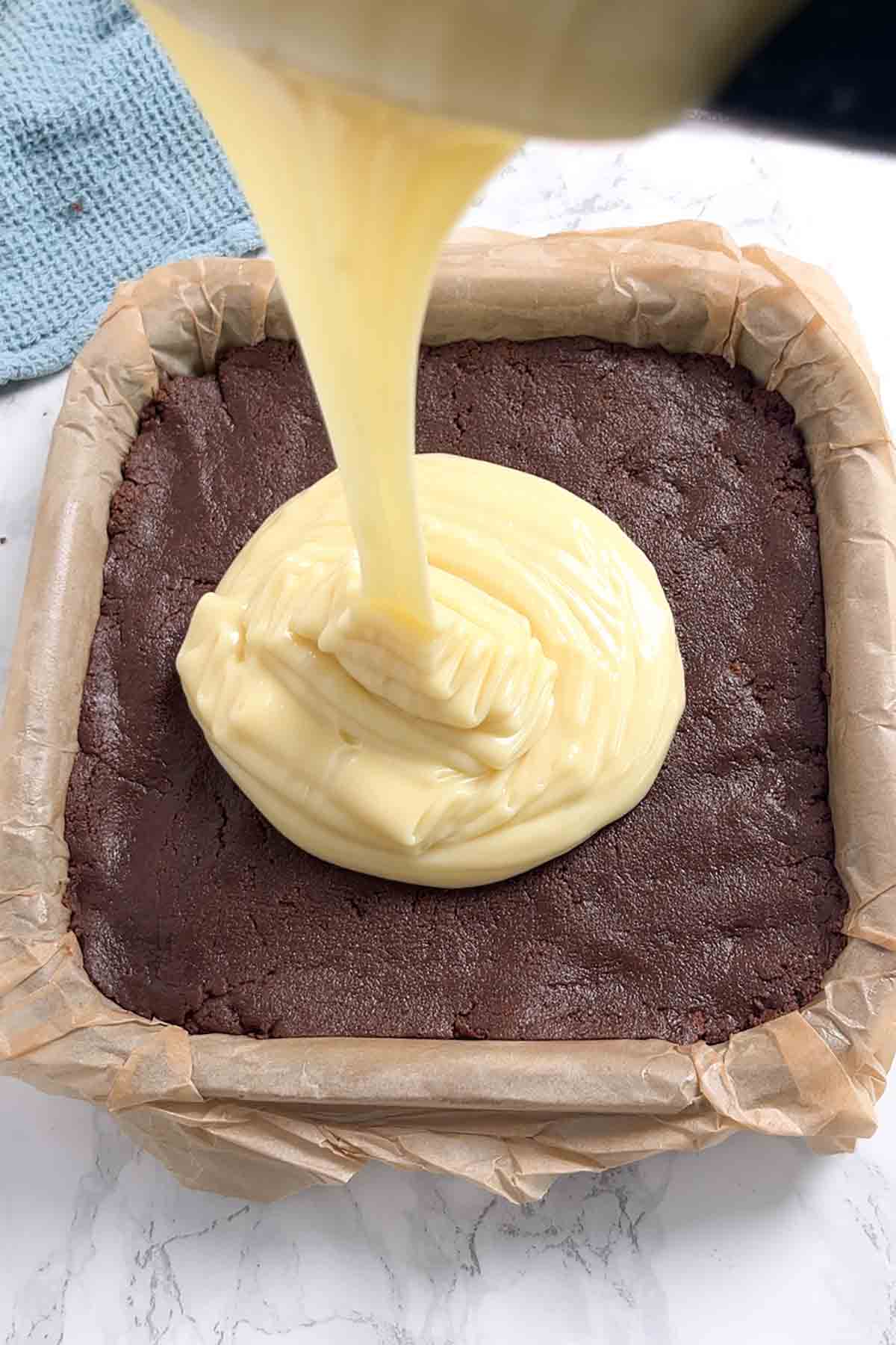 white chocolate fudge topping being poured onto chocolate biscuit base