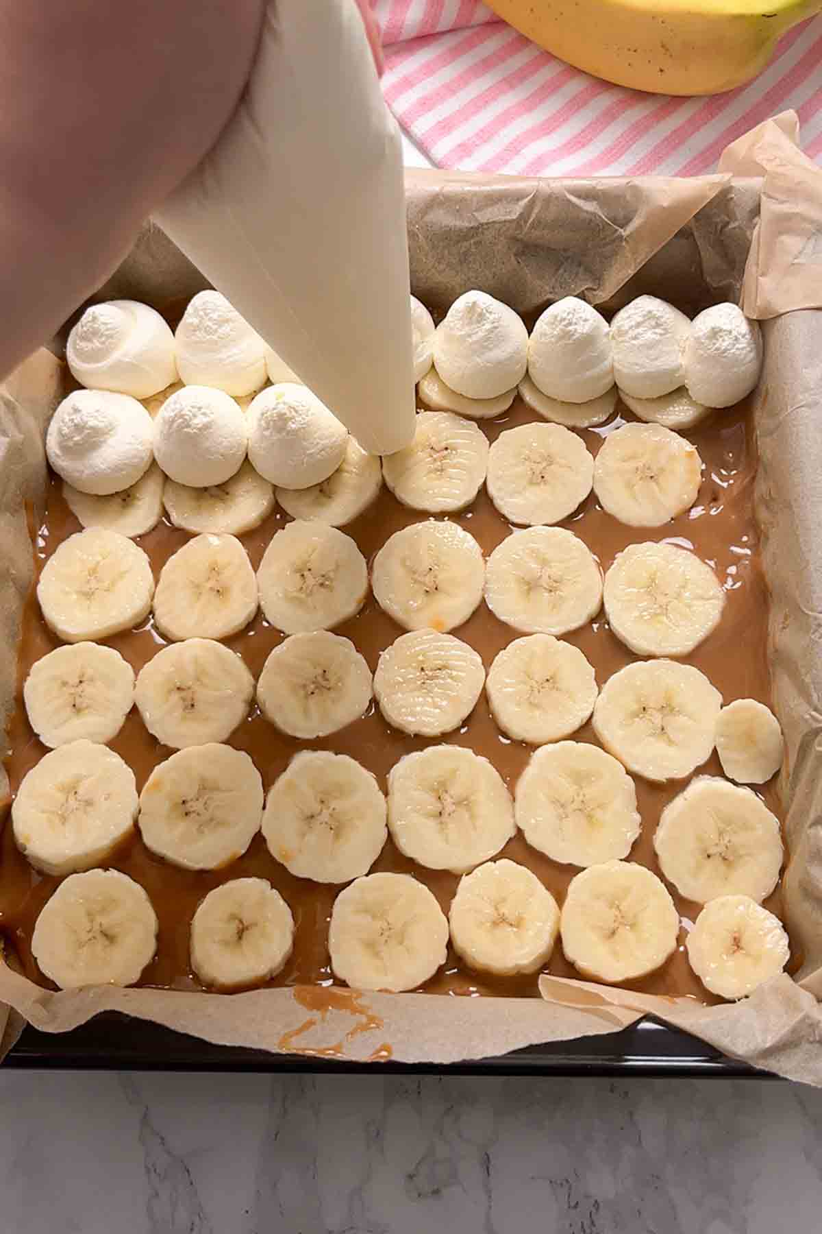 piping whipped cream on top of the caramel and bananas