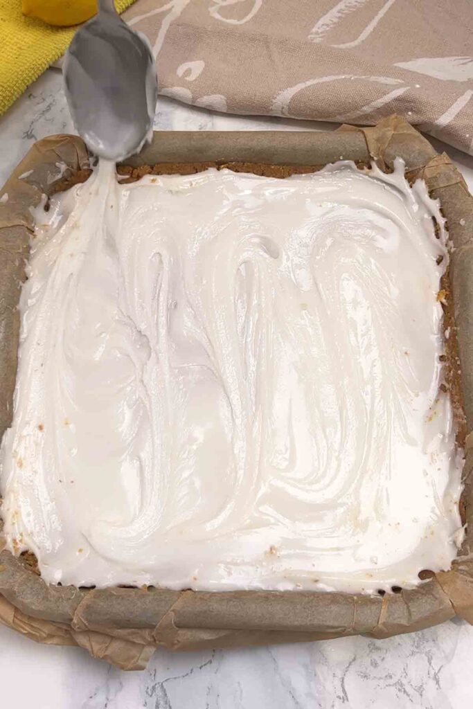 spreading white icing on top of the biscuit base